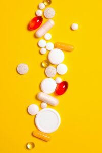Colorful pills and tablets scattered on a vivid yellow background, symbolizing medicine and health.